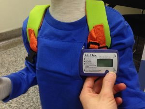 A small device held beside a pocket sewn into the front of a child's shirt meant to hold it